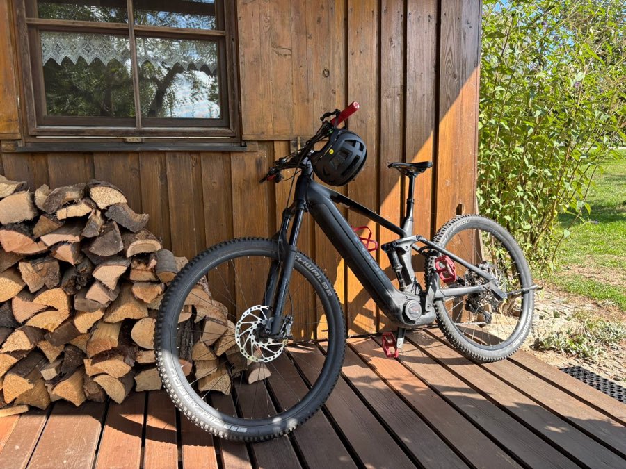 E-Mountainbike lehnt an der Holzwand des Ferienhauses neben einem Stapel Brennholz