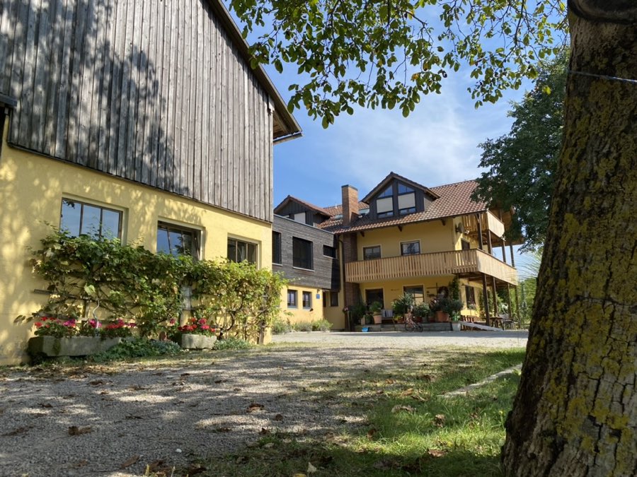 Hofeinfahrt mit gelbem Wohnhaus, Holzbalkon und Scheune, im Vordergrund ein Nussbaum