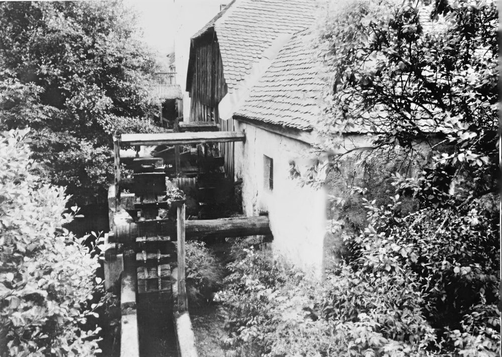 Historische Aufnahme der Hammerschmiede in Seebarnhammer mit hölzernen Wasserrädern am Mühlgraben neben einem weiß getünchten Haus